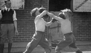 Black and white photo of two young boys with boxing gloves, punching each other