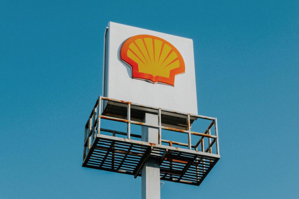 A large white sign displaying the Shell corporation logo sits above a metal pole against a blue background.