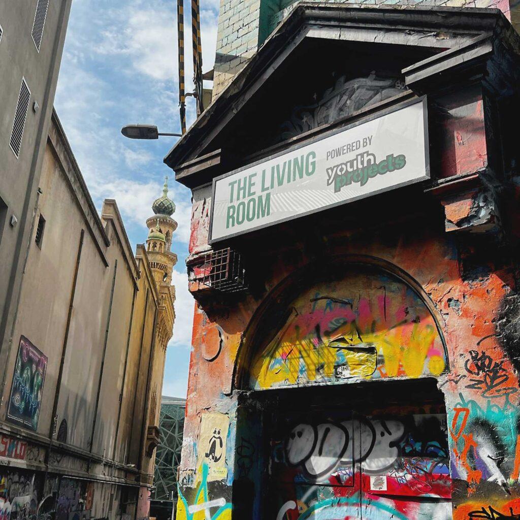 An image of the exterior Living Room run by Youth Projects, a drop-in centre located in Hosier Lane for those experiencing homelessness. The door is coloured in bright graffiti.